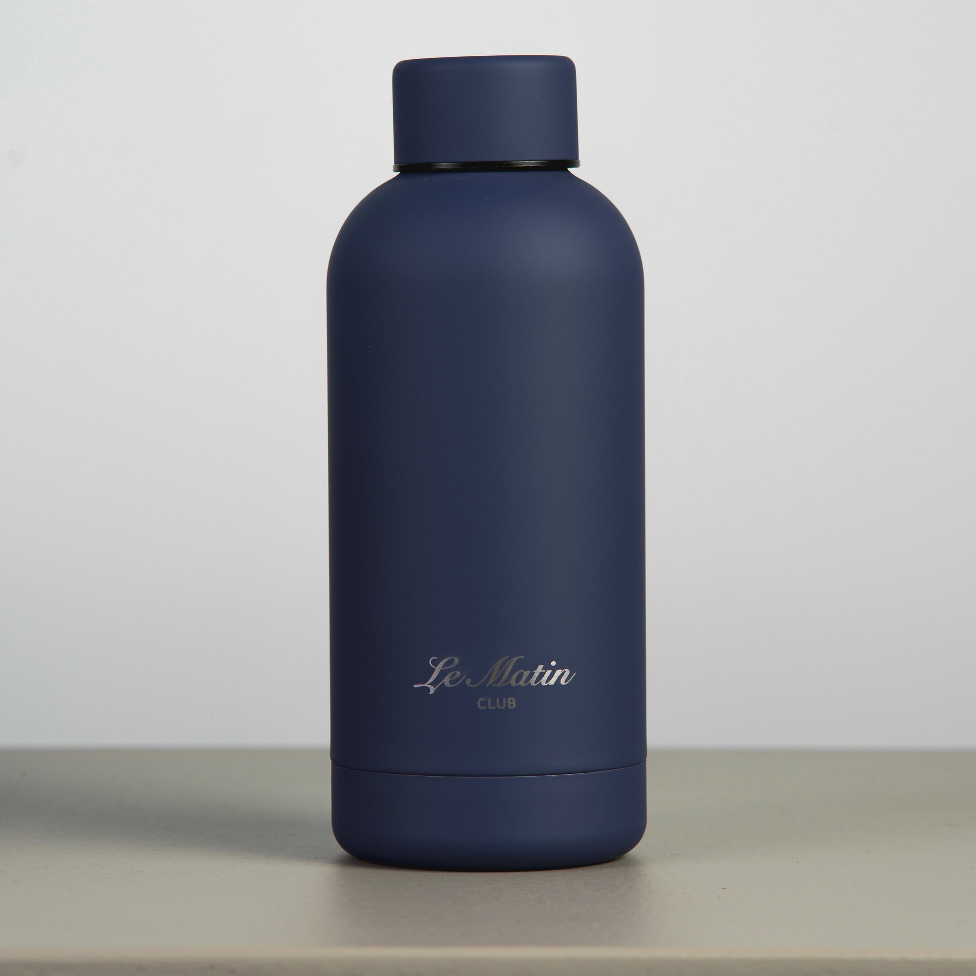 Navy blue water bottle with 'Le Matin' branding on a light gray background