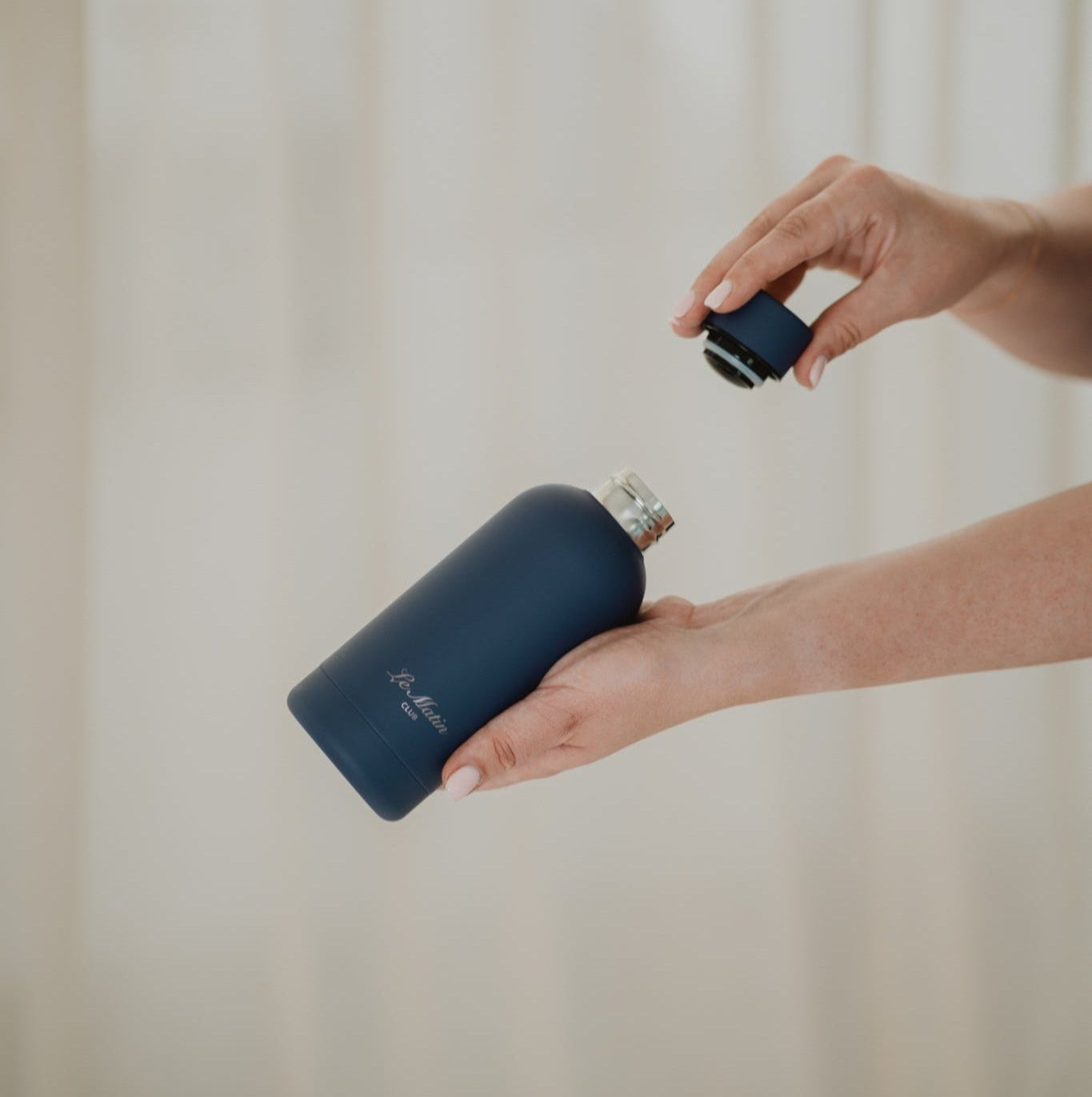 Person holding a navy blue water bottle with a beige background
