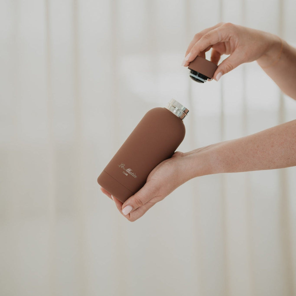 Person holding a brown water bottle against a neutral background