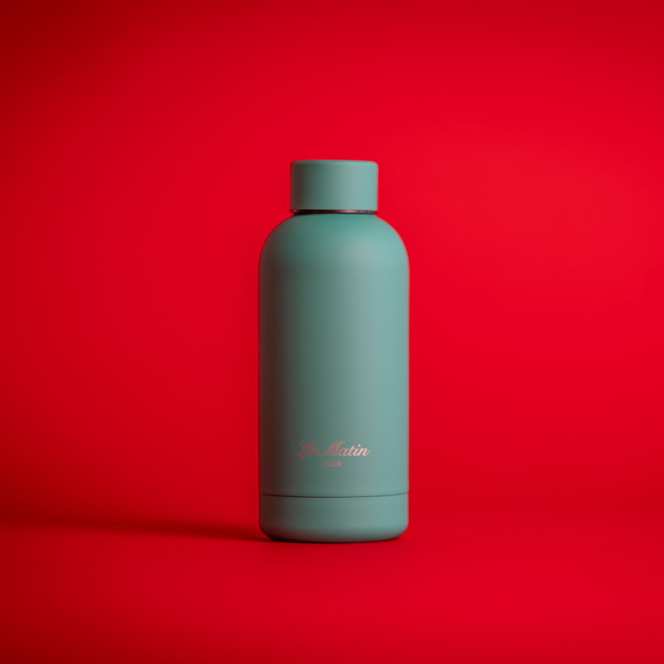 Greeb water bottle with 'Le Matin' branding on a red background