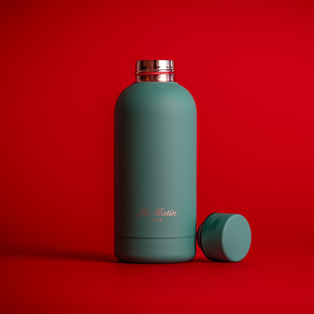 Green water bottle with silver cap on a light gray background