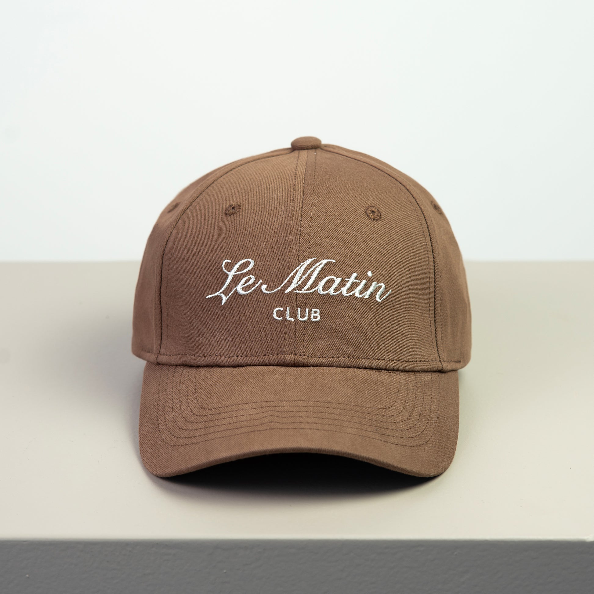 Brown cap with 'Le Matin Club'embroided  text on a white background