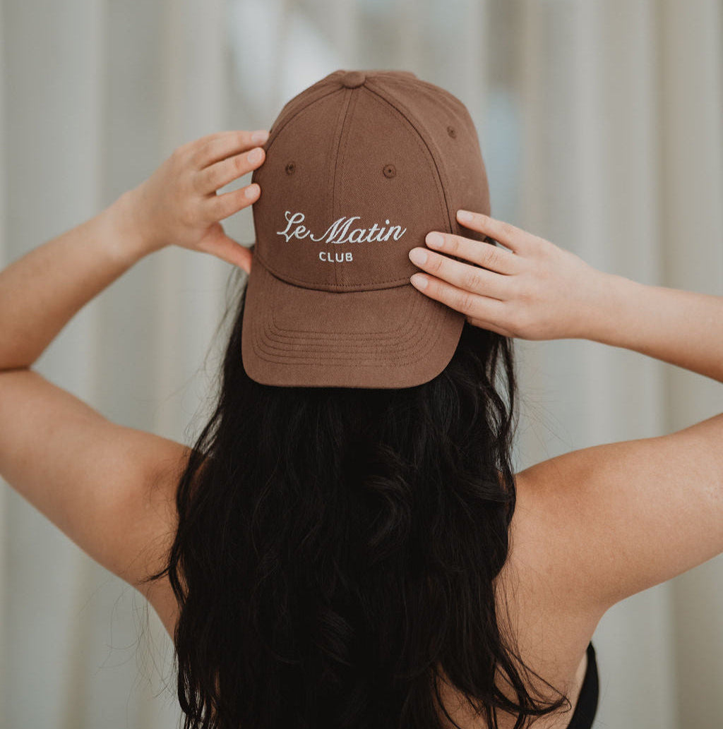 Girl wearing a brown cap with 'Le Matin Club' text against a neutral background