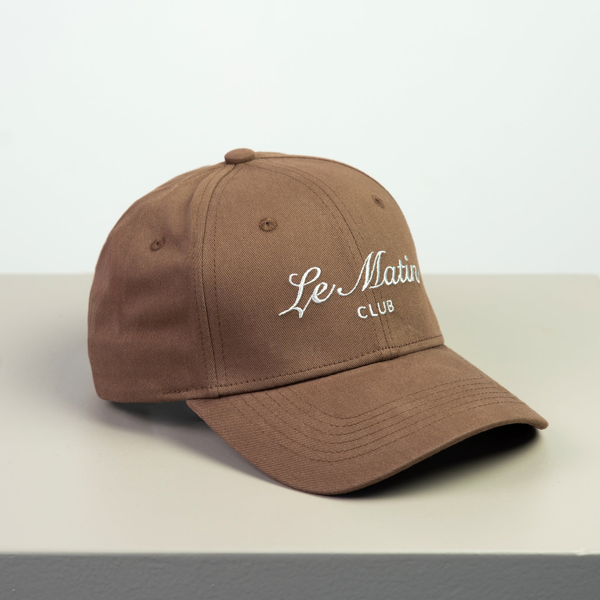Brown cap with 'Le Matin Club' embroided text on a light gray background