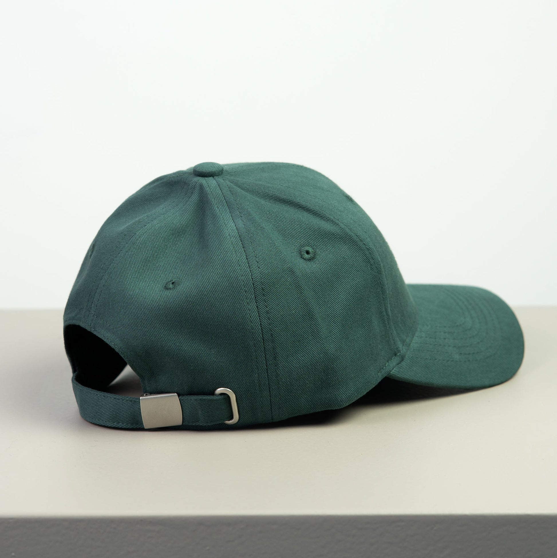 Green baseball cap with adjustable metal buckle on a white surface with a light gray background