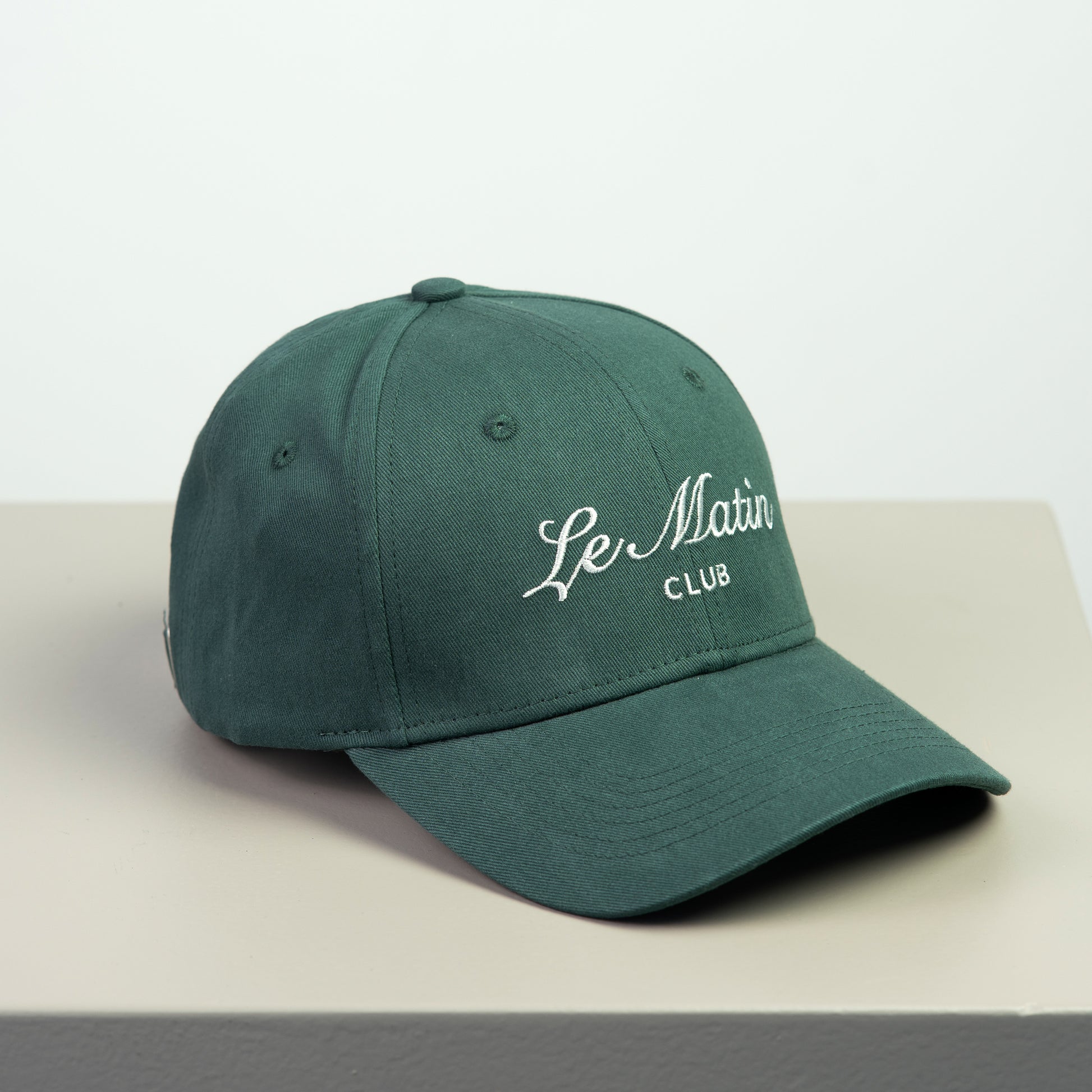 Green cap with 'Le Matin Club' embroided  text on a light gray background