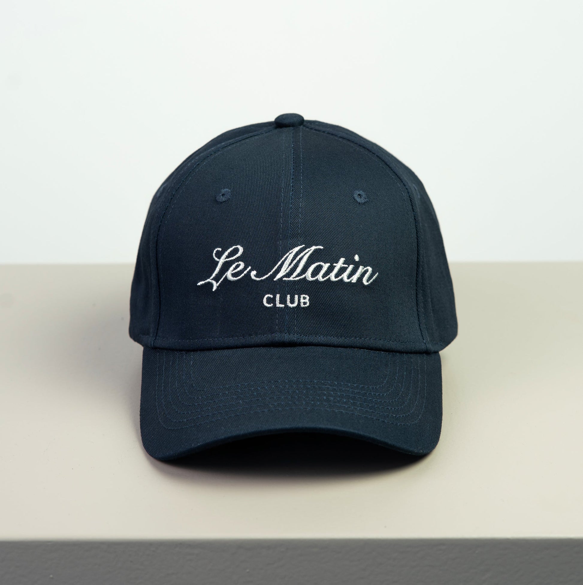 Navy blue cap with 'Le Matin Club' embroidery on a light gray background