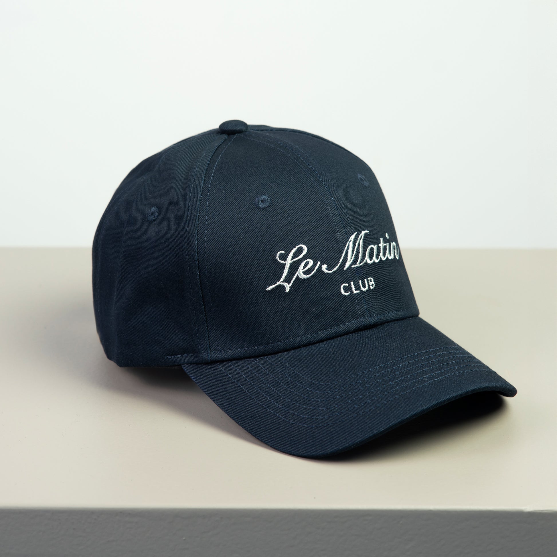 Navy blue cap with 'Le Matin Club' embroided text on a light gray background