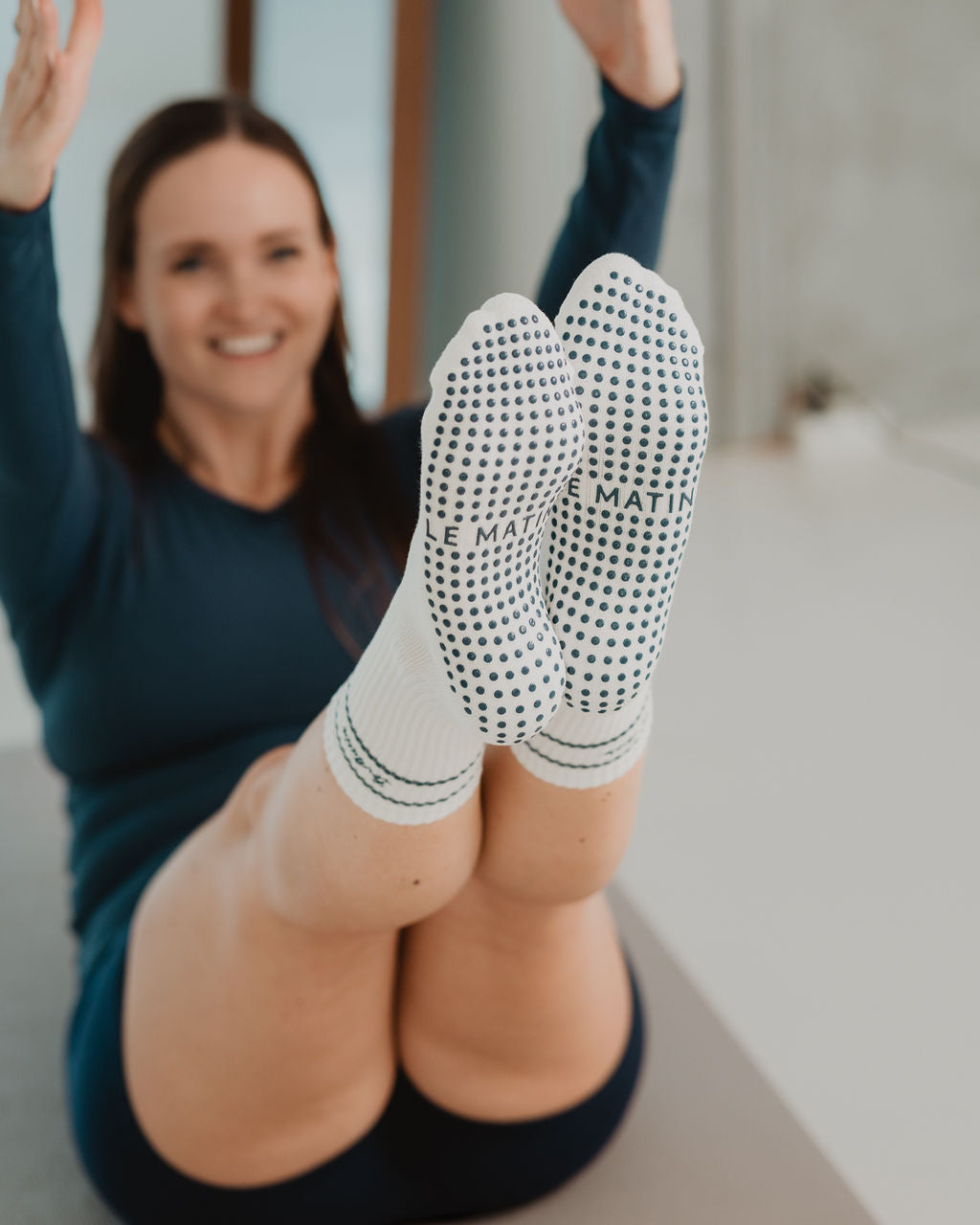 Person wearing white socks with navy patterns, sitting on a yoga mat indoors.