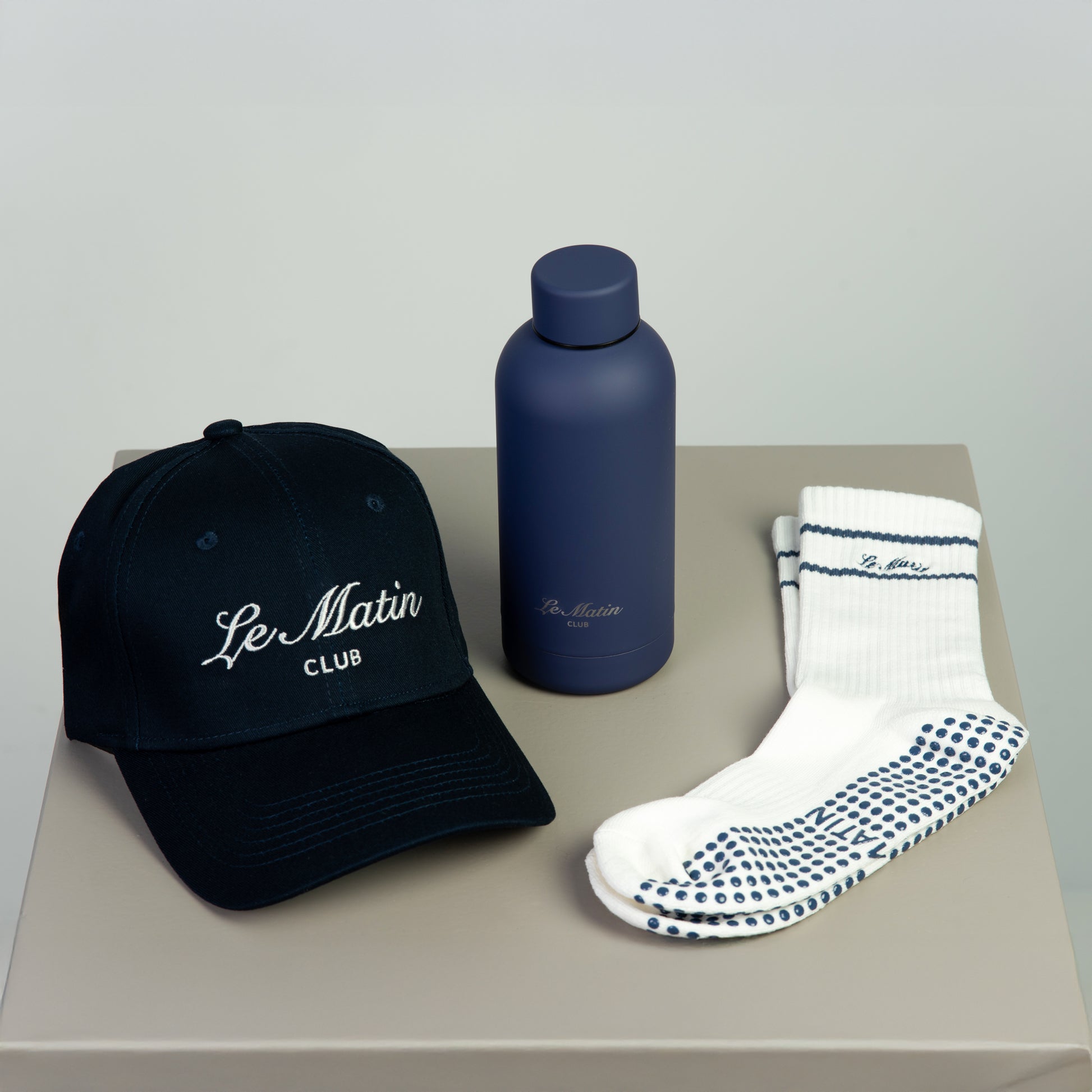 Navy cap, blue water bottle, and white socks with navy patterns on a beige surface.
