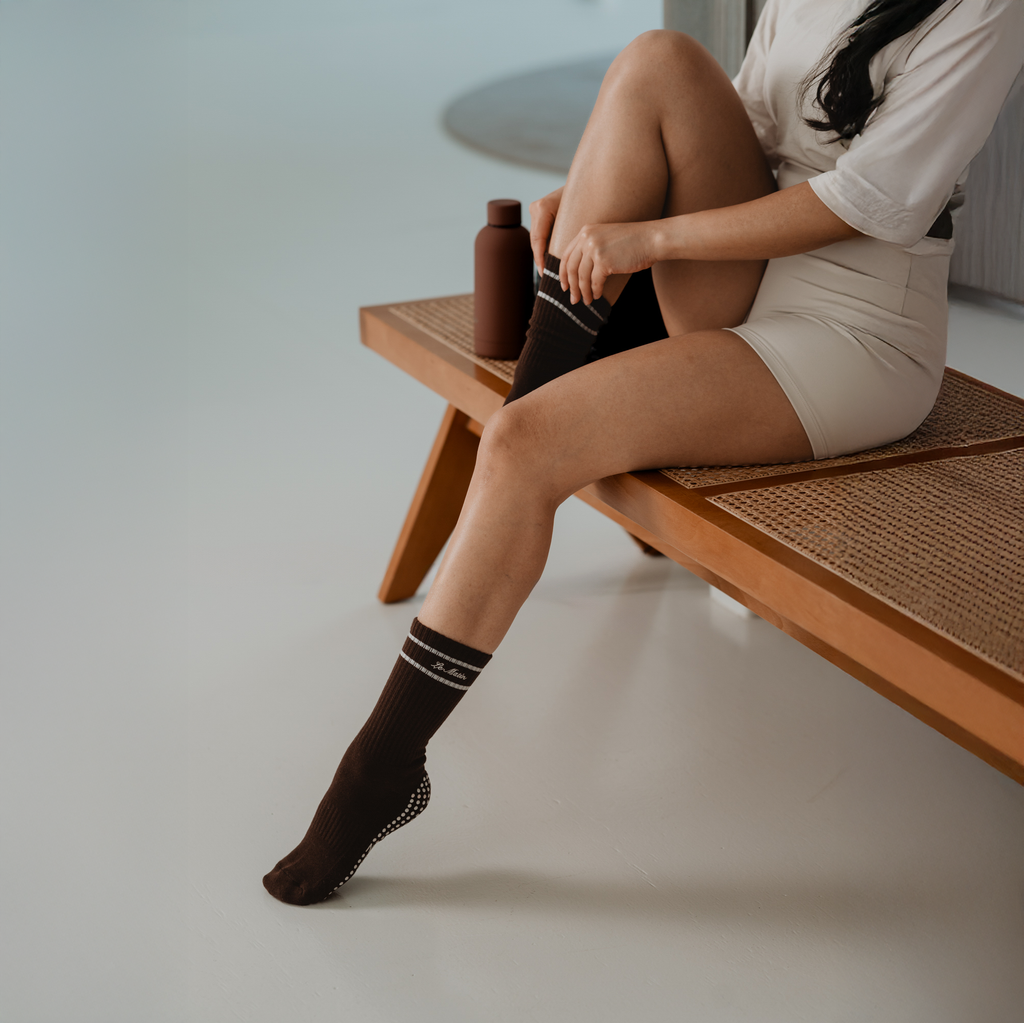 Person sitting on a wooden bench wearing brown Le Matin socks with Grey stripes.